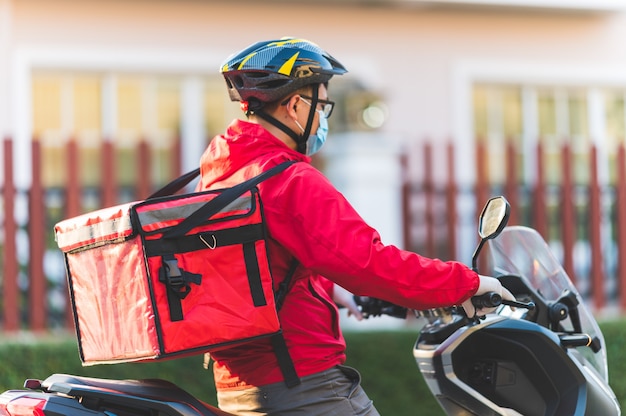 Junger mann, der für einen lebensmittel-lieferservice arbeitet, der mit straßenmotorrad in der stadt prüft