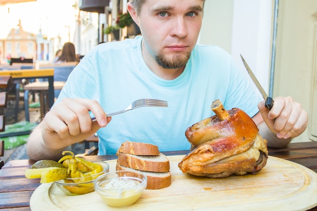 Junger Mann, der geräuchertes Schweinekeulenfleisch isst und Bier trinkt