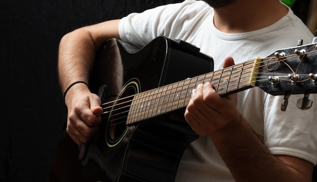 Junger Mann, der Gitarre spielt, Nahaufnahme dunkler Hintergrund