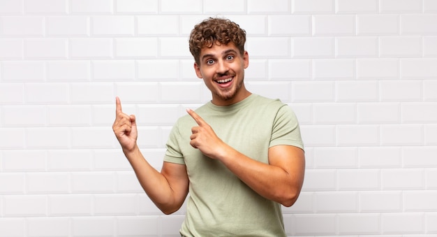 Junger Mann, der glücklich lächelt und zur Seite und nach oben zeigt, wobei beide Hände Objekt im Kopierraum zeigen