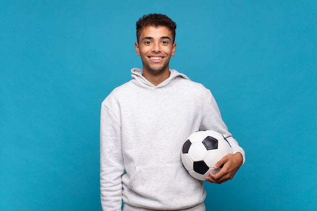 Junger Mann, der glücklich mit einer Hand auf Hüfte und selbstbewusster, positiver, stolzer und freundlicher Haltung lächelt. Fußballkonzept