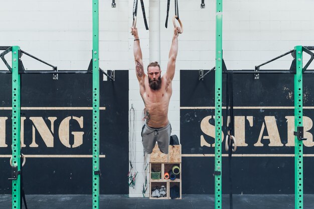 Junger Mann, der gymnastische Innenringe crossfit Turnhalle ausbildet