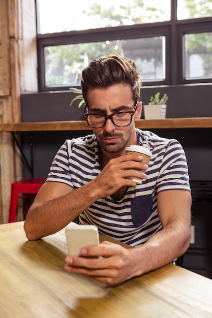 Junger Mann, der Handy in der Cafeteria verwendet