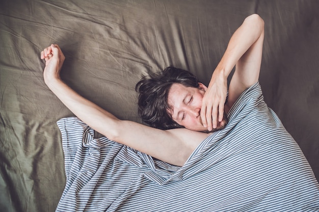 Junger Mann, der im Bett unter einer Decke liegt