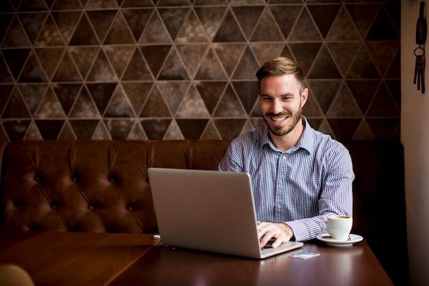 Junger Mann, der im Café sitzt und Laptop verwendet