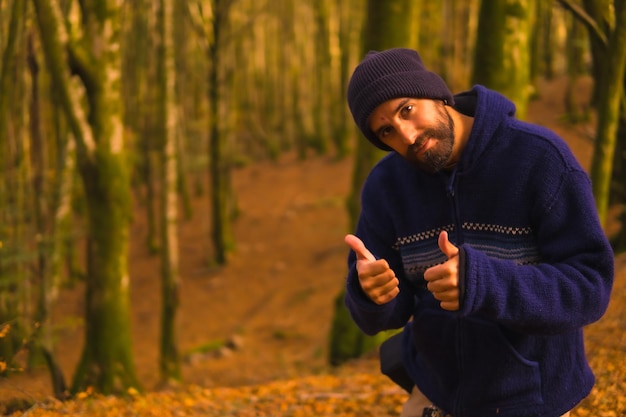 Junger Mann, der im Herbst im goldenen, schönen Wald Daumen hochgibt