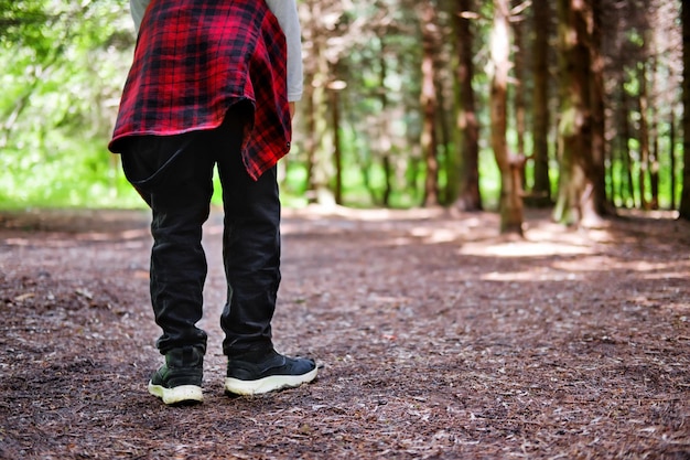 Junger Mann, der im Park spazieren geht Nahaufnahme der Beine des Mannes in Jeans und schwarzen Lederstiefeln mit Sonnenlicht vor dem Hintergrund der Naturunschärfe