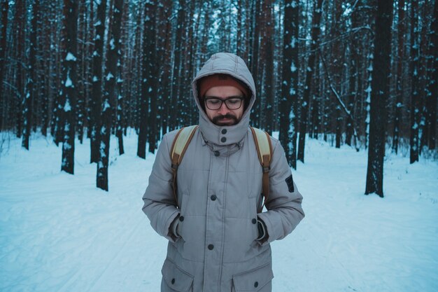 Junger Mann, der im schneebedeckten Wald des Winters steht