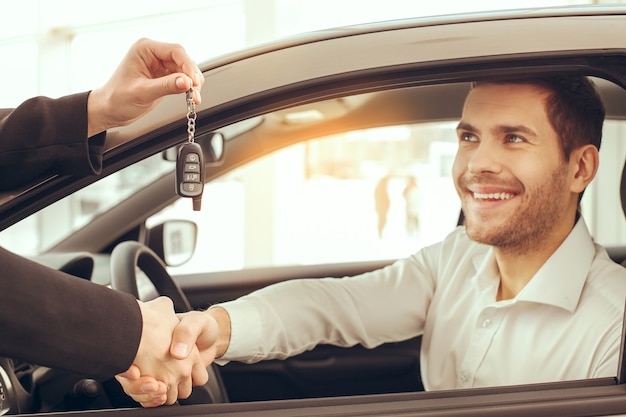 Junger Mann, der in der Nähe des Autos steht und den Schlüsselverleih bekommt