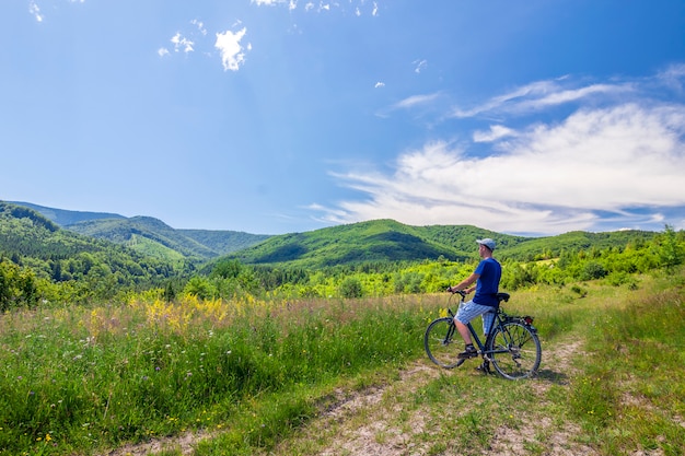 Junger Mann, der in der Nähe von Fahrrad im Morgensonnenaufgang mit wunderbaren Strahlen und Morgennebel während des ruhigen Sommeraktivtages steht