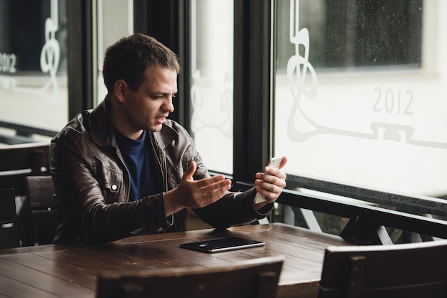 Junger Mann, der in einem Café mit einer Tablette auf dem Tisch sitzt