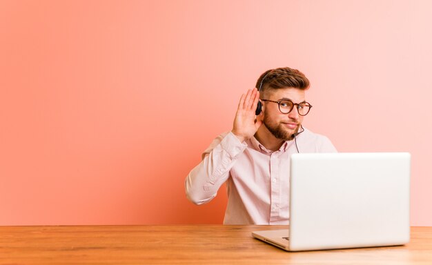 Junger Mann, der in einem Callcenter arbeitet und versucht, einen Klatsch zu hören.