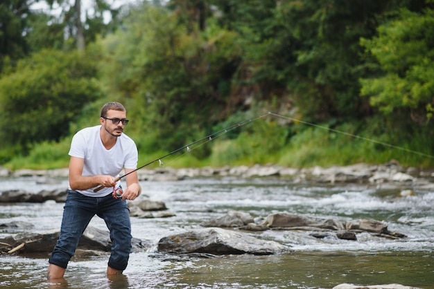 Junger Mann, der in einem Fluss fischt