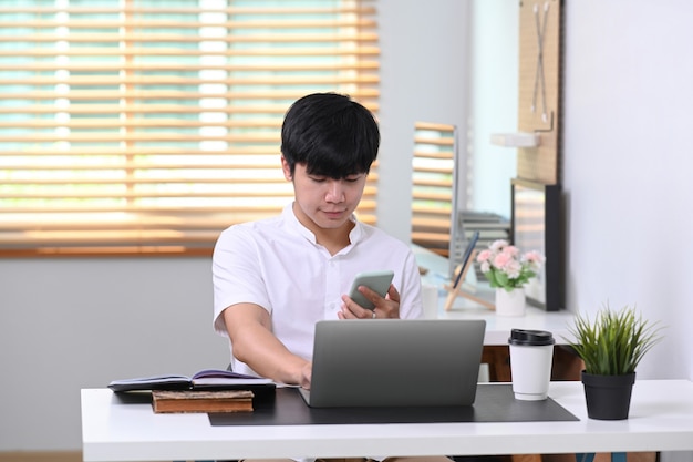 Junger Mann, der in einem komfortablen Büro sitzt und ein Smartphone verwendet.