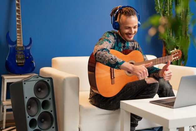 Junger Mann, der in seinem Zimmer sitzt und Gitarrentutorial auf Laptop hautnah betrachtet