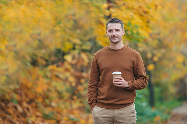 Junger Mann, der Kaffee im Herbstpark draußen trinkt