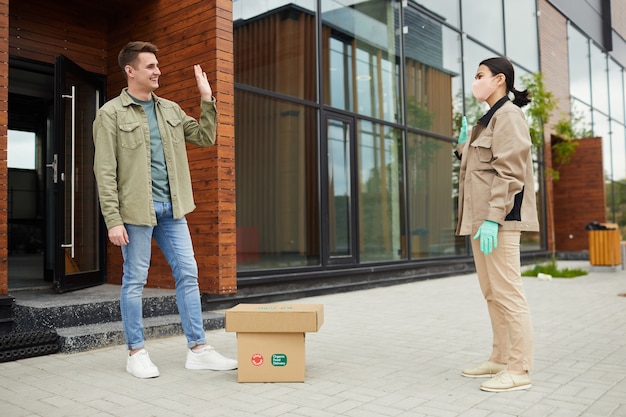 Junger Mann, der kontaktloses Lieferpaket von der Lieferfrau im Freien erhält