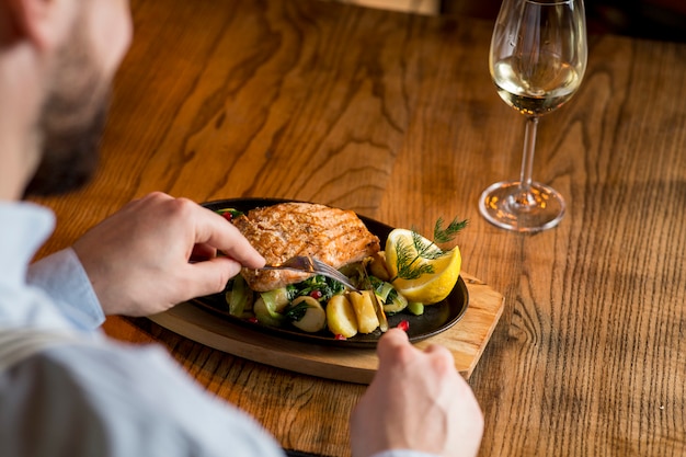 Junger Mann, der Lachsfilet mit überbackenen Kartoffeln, Lauch und Spinat isst