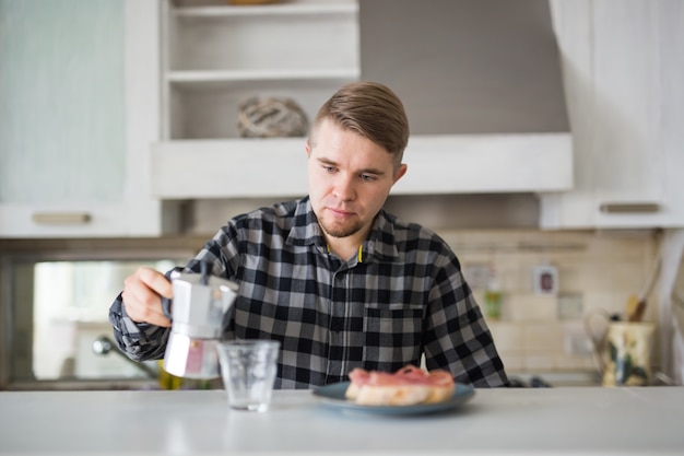 Junger Mann, der lächelt und eine Tasse Kaffee in der Küche hält