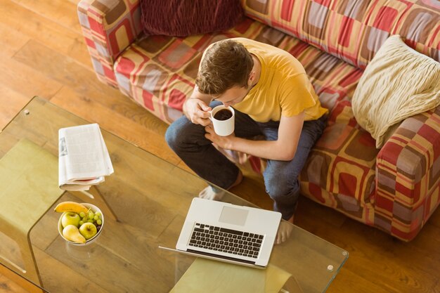 Junger Mann, der Laptop auf seiner Couch verwendet