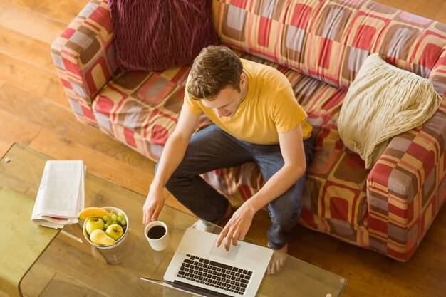 Junger Mann, der Laptop auf seiner Couch verwendet