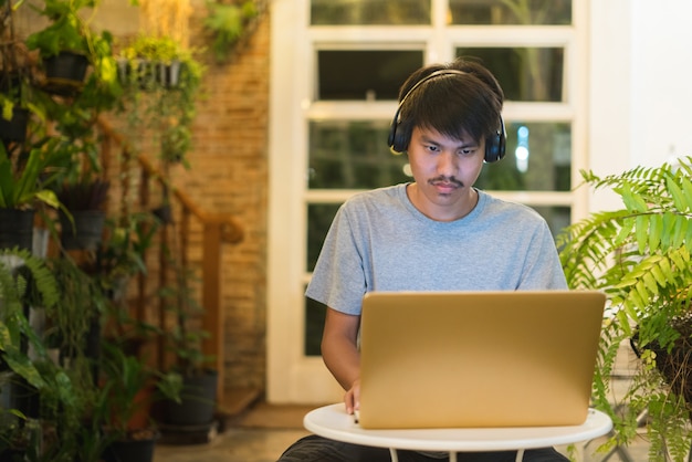 Junger Mann, der Laptop verwendet, der Musik auf Kopfhörer hört