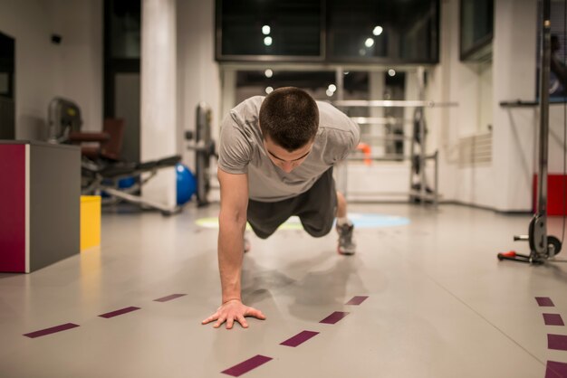 Junger Mann, der Liegestütze an einer Hand im Fitnessstudio tut