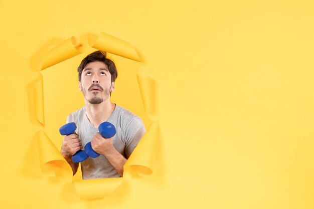 junger Mann, der mit blauen Hanteln auf gelbem Hintergrund trainiert Sporthalle Übung fit