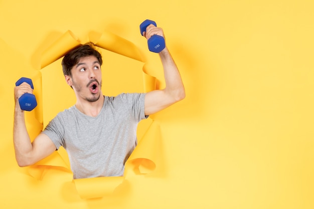 junger Mann, der mit blauen Hanteln auf gelbem Hintergrund trainiert, trainiert Athlet Sport Gym