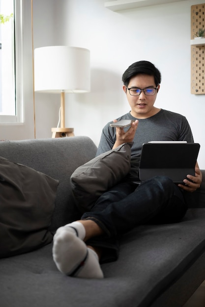 Junger Mann, der mit Computertablette arbeitet und im Wohnzimmer am Handy spricht.