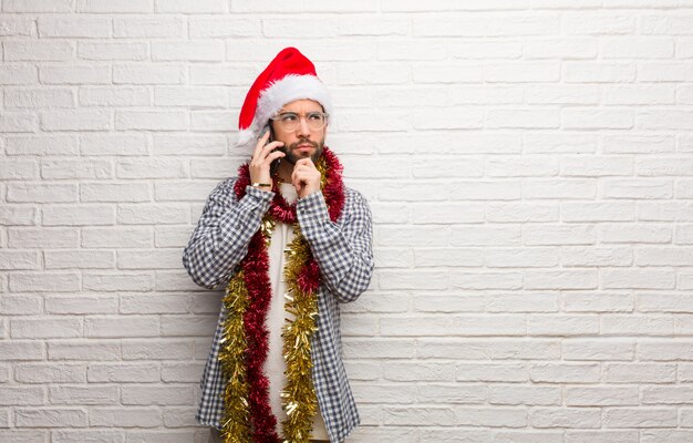 Junger Mann, der mit den Geschenken feiert das zweifelnde Weihnachten und verwirrt sitzt