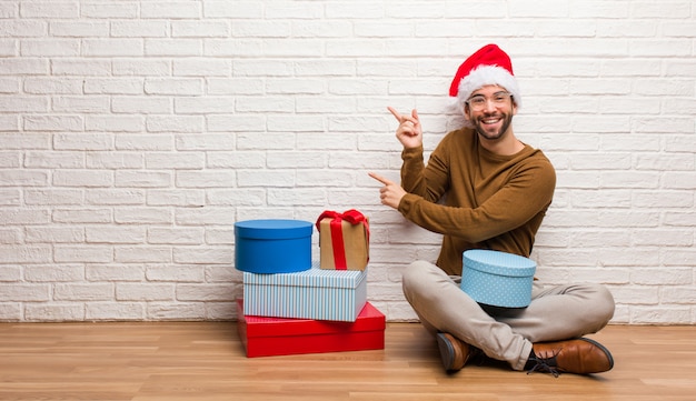 Junger Mann, der mit den Geschenken feiert Weihnachten feiert, zeigend auf die Seite mit dem Finger