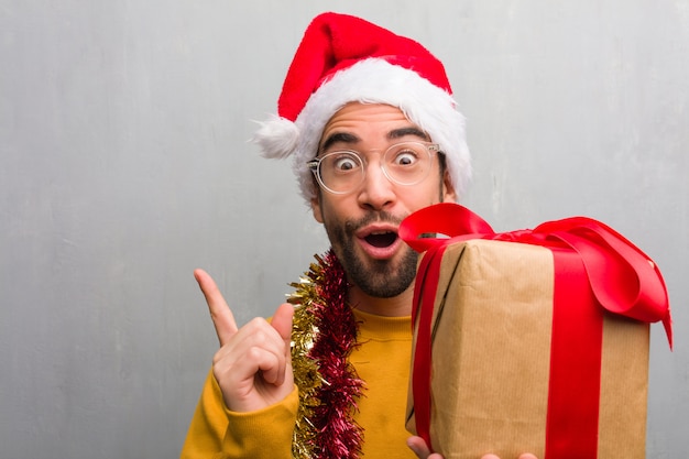 Junger Mann, der mit den Geschenken feiert Weihnachten feiert, zeigend auf die Seite mit dem Finger