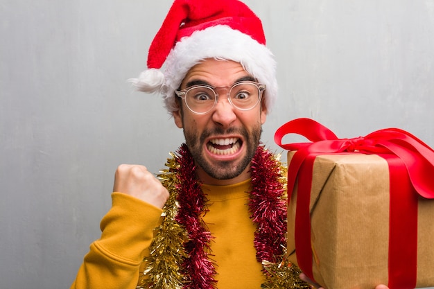 Junger Mann, der mit den Geschenken feiert Weihnachten sitzt, sehr verärgert und aggressiv schreiend