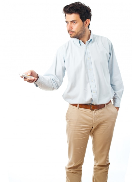 Junger Mann, der mit einer Fernbedienung auf einem weißen Hintergrund zeigt