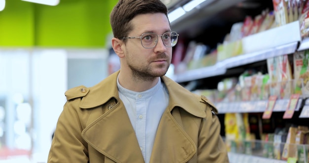 Junger Mann, der mit Einkaufswagen im Supermarkt spazieren geht Stilvoller Mann, der Einkaufswagen mit Produkten schiebt Großer Laden mit vielen Gängen