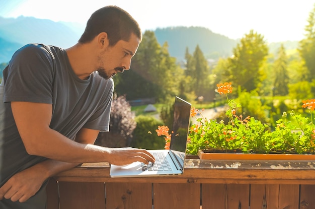 Junger Mann, der mit Laptop auf landschaftlich schönem Berghintergrund arbeitet Attraktiver Mann, der freiberuflich arbeitet