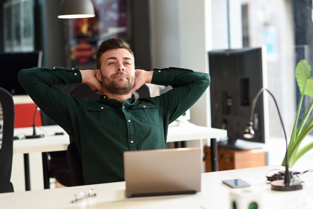 Junger Mann, der mit Laptop-Computer auf weißem Schreibtisch studiert.