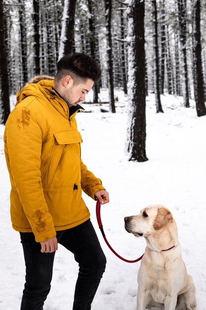 Junger Mann, der mit seinem Hund an einem schneebedeckten Berg spielt