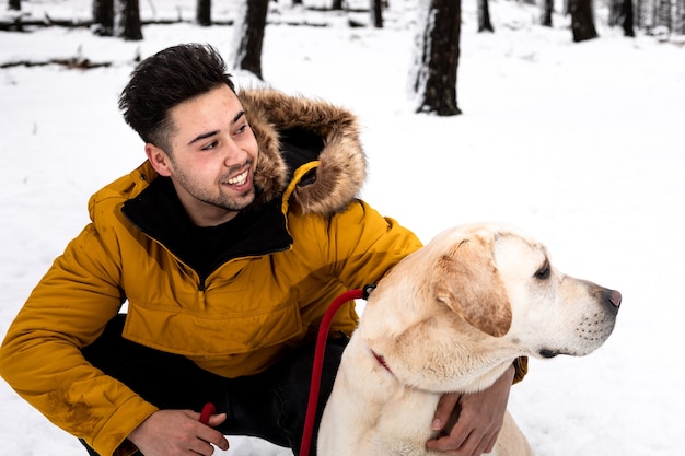 Junger Mann, der mit seinem Hund an einem schneebedeckten Berg spielt