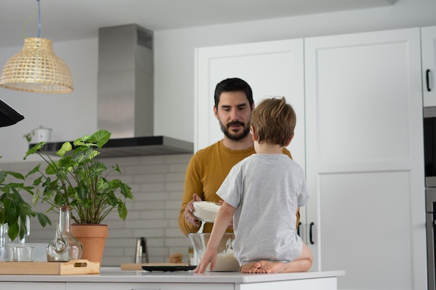 junger mann, der mit seinem sohn in seiner hausküche selbstgebackenes brot macht