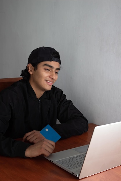 Junger Mann, der mit seiner Kreditkarte einen Online-Kauf auf seinem Computer tätigt