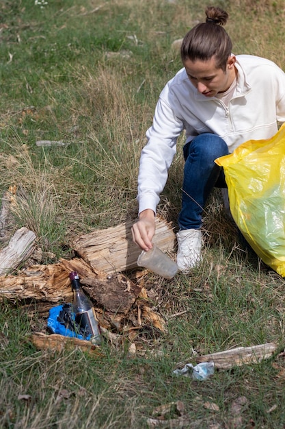 Junger Mann, der nach einer Party Müllplastikbecher und Glasflaschen mit Alkohol aufsammelt