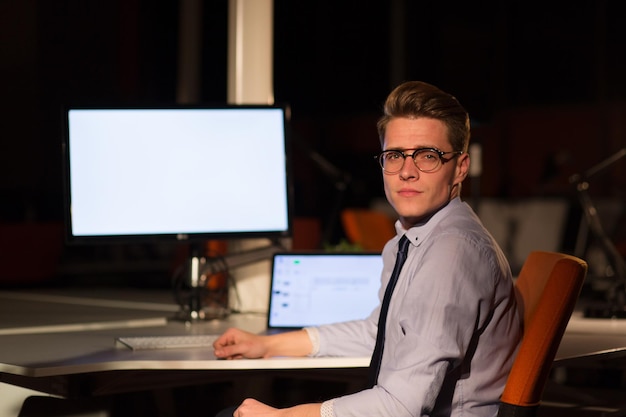 Junger Mann, der nachts im dunklen Büro am Computer arbeitet. Der Designer arbeitet in der späteren Zeit.