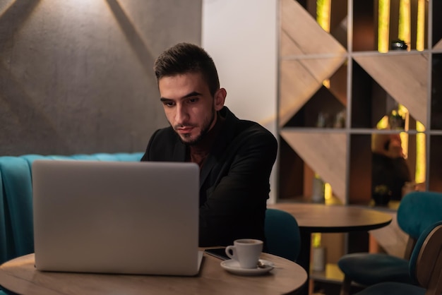 Junger Mann, der nachts in seinem Büro an einem Laptop arbeitet