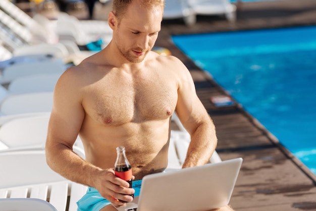 Junger Mann, der nahe Schwimmbad steht und eine große Zeit hat