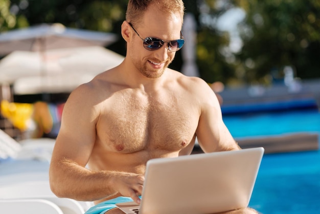 Junger Mann, der nahe Schwimmbad steht und eine große Zeit hat