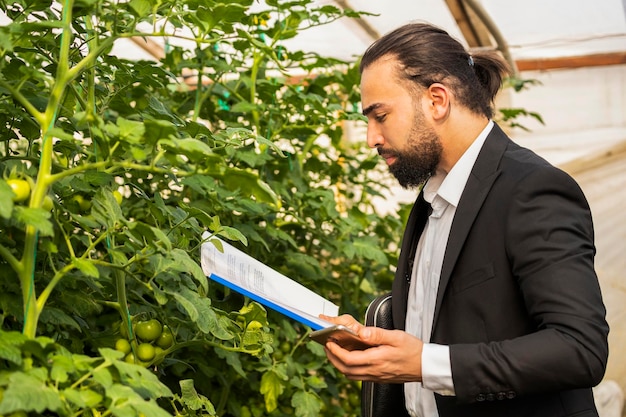 Junger Mann, der Notizbuch hält und am Gewächshaus steht