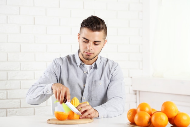 Junger Mann, der Orangen schneidet und Orangensaft vorbereitet