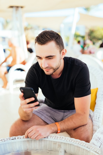 Junger Mann, der per Handy im Außencafé am Sommerresort am Strand anruft